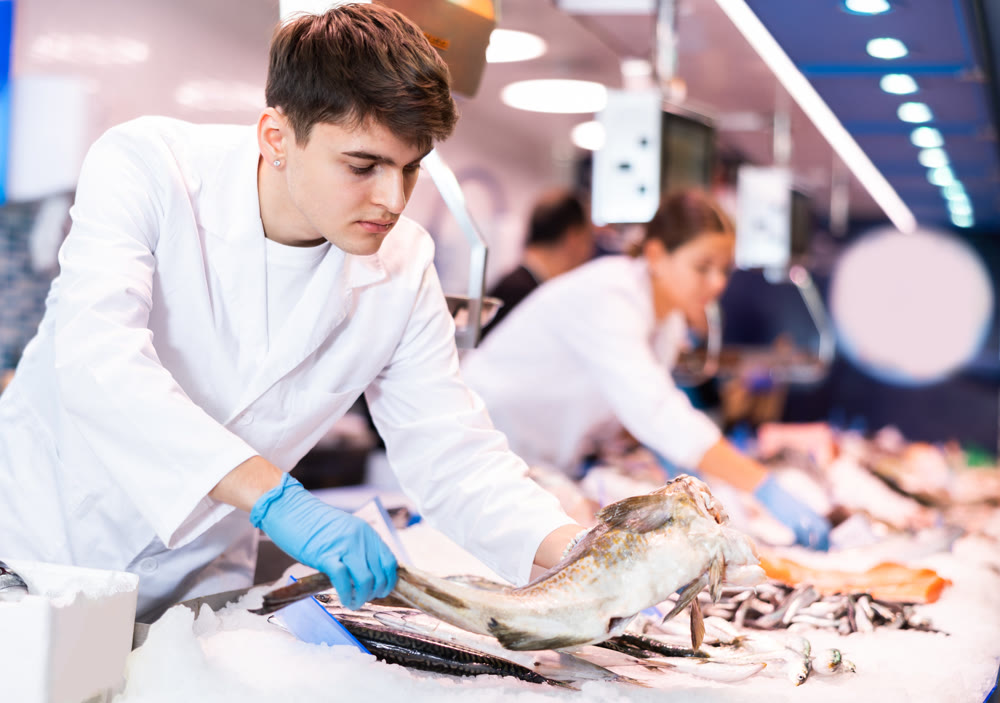 Positive salesman demonstrating cod in fish store