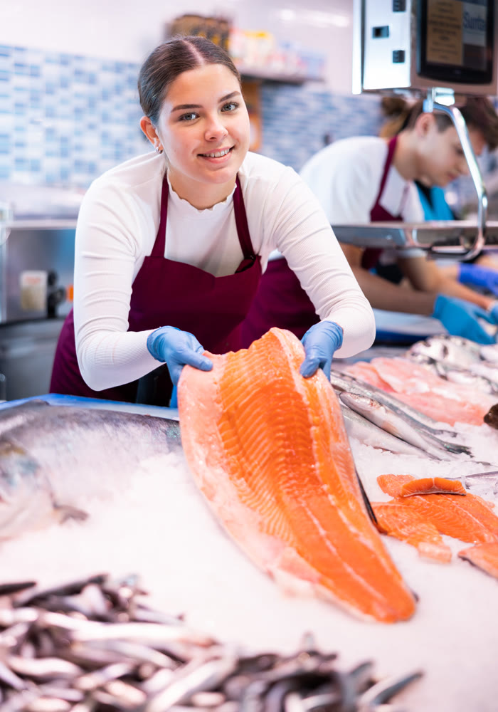 Seller in apron standing near counter offering fresh fish pink salmon