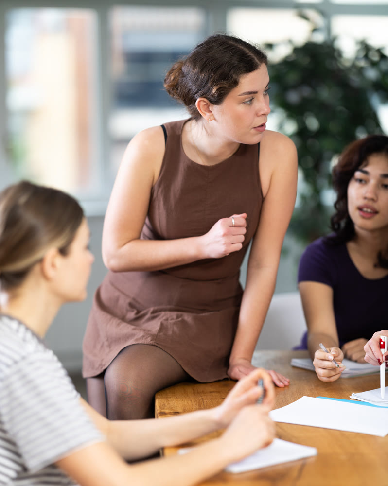 Young woman sitting on table during group discussion with diverse ladies