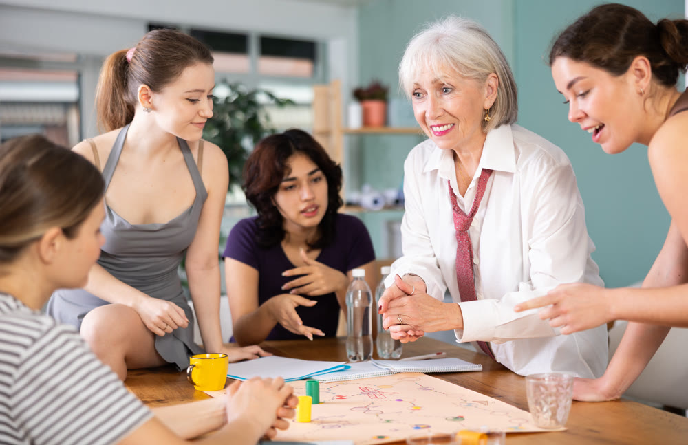 Emotional female colleagues of business company different ages playing exciting board game in office