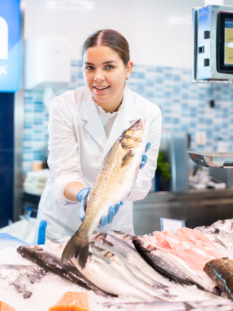 Positive saleswoman demonstrating seabass in fish store