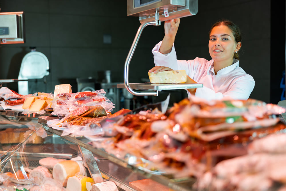 Young woman weighing cheese at counter