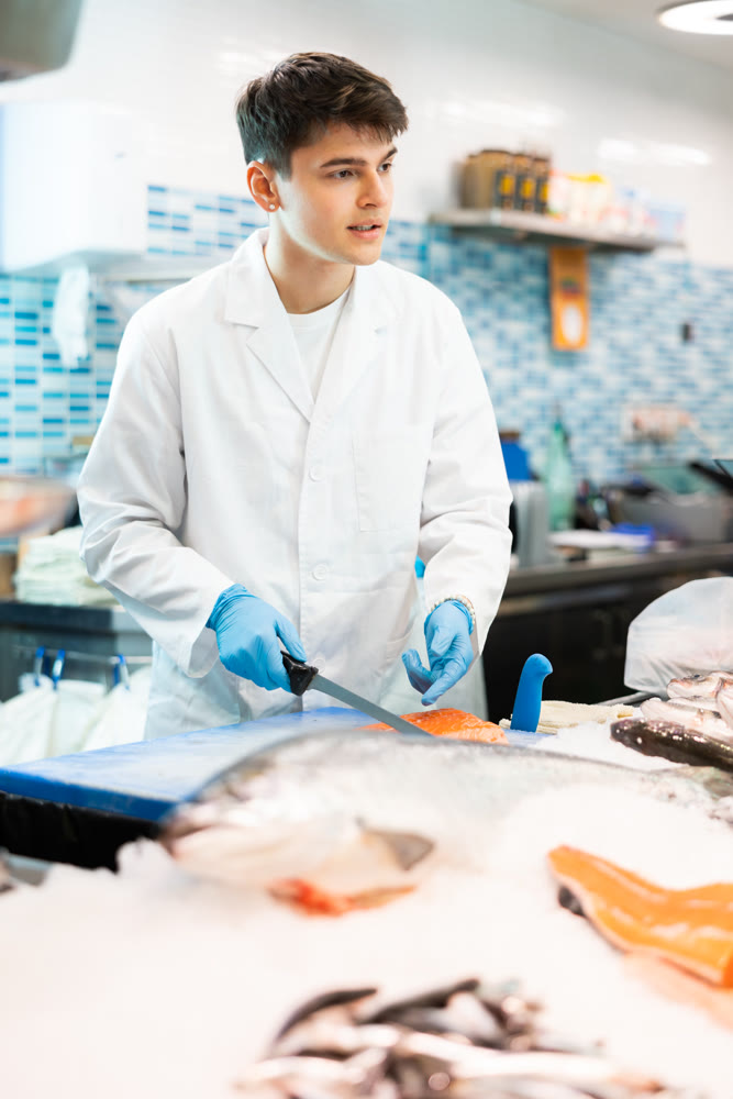 Seller with knife cut fish in supermarket near counter