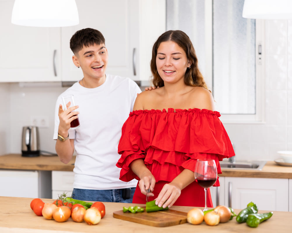 Young happy married couple with glasses of wine preparing a festive dinner