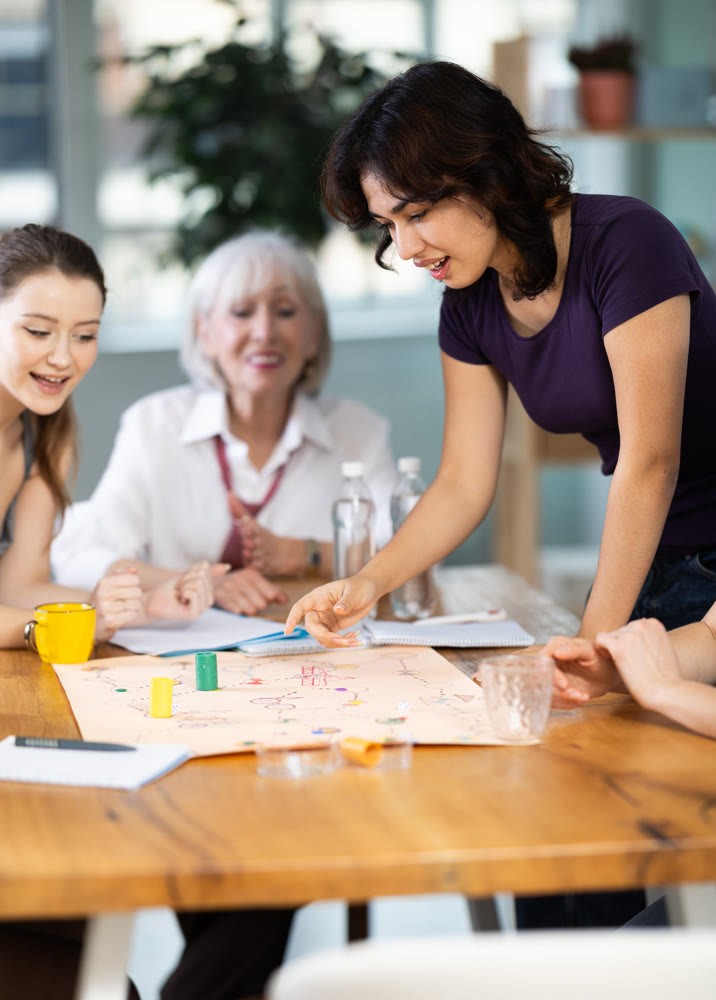 Emotional female colleagues of business company different ages playing exciting board game in office