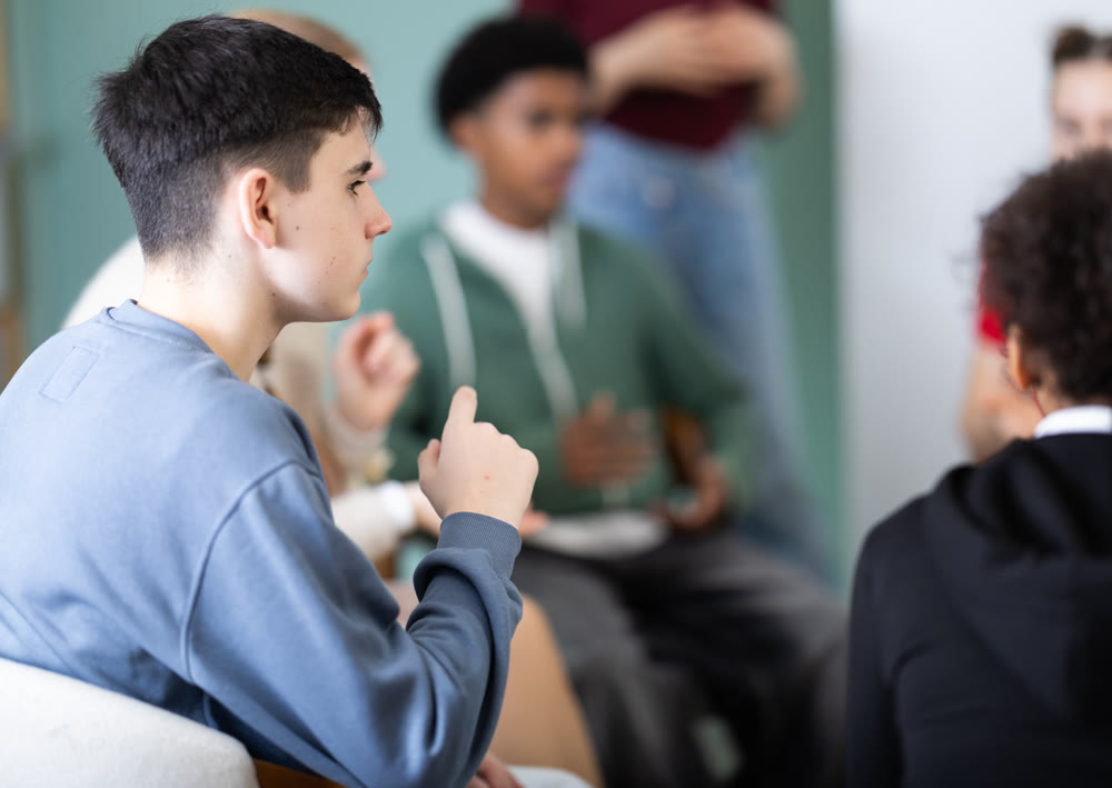 Teen pupils gathering in circle, participate at speaking club with coach, teacher watching.