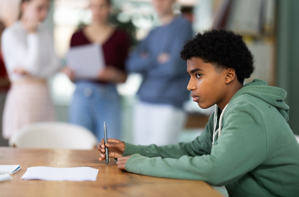 Upset young male student sitting alone at desk