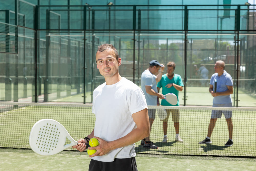 Portrait of sporty male padel player with a racket and ball in his hands on the background of tennis court