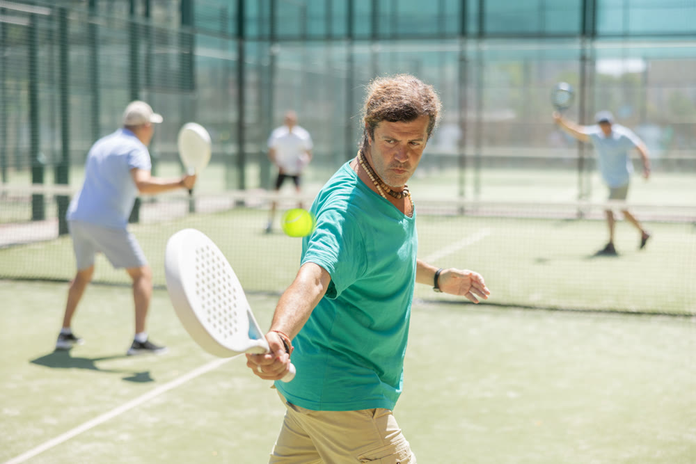 Adult and elderly men playing padel against two men