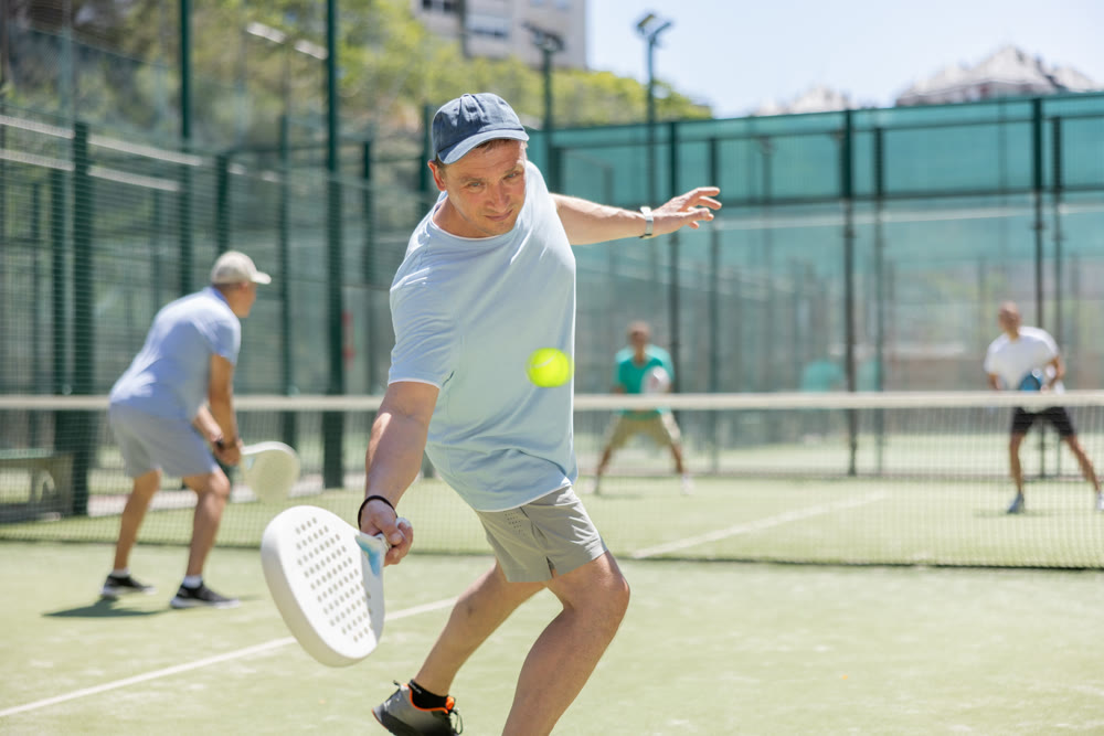 Padel game - man with partners plays on court