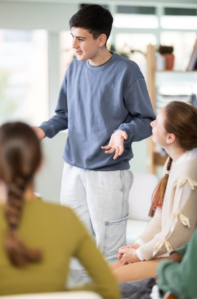 Teen group sit in circle and listen to Caucasian boy classmate speaking