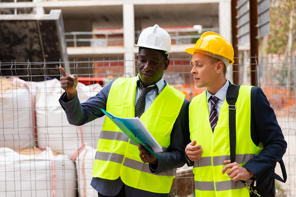African-american engineer discussing a construction plan with a colleague shows him something