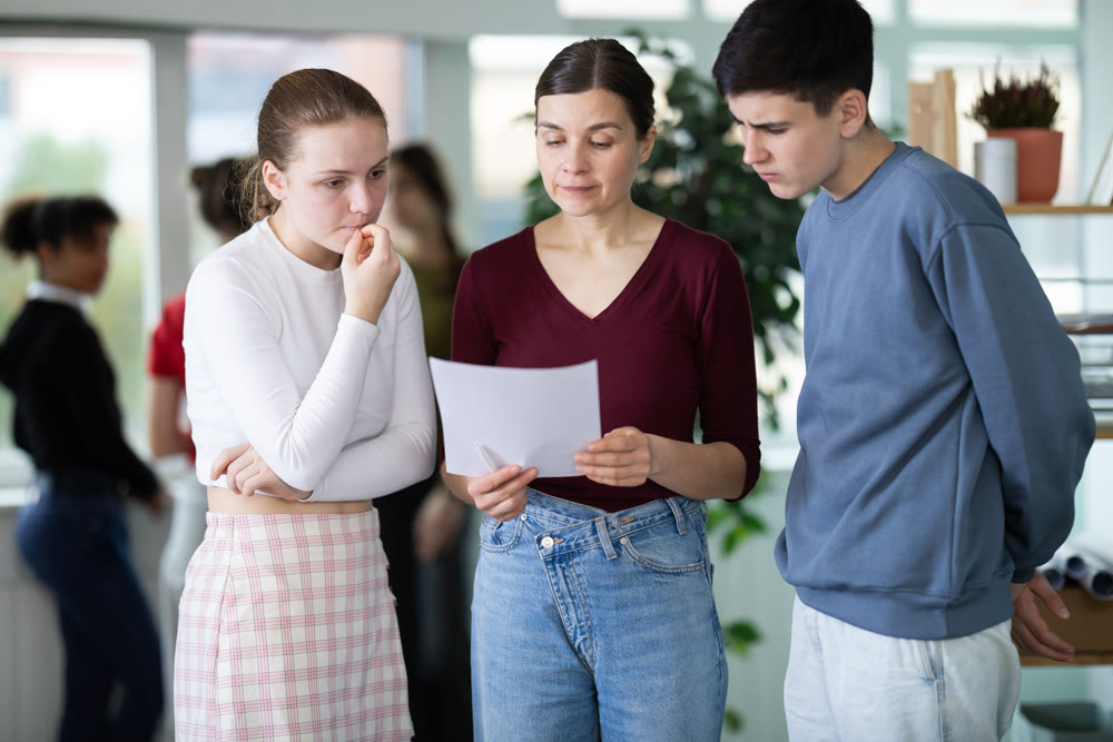 Female teacher holds papers in her hands and gives a task to schoolchildren