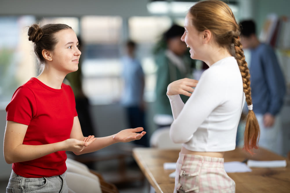 Two teenage girls communicate in a circle in a school