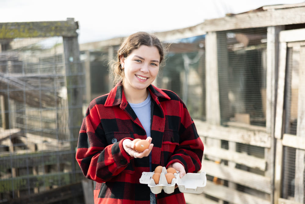 Young woman with chicken eggs in hen house