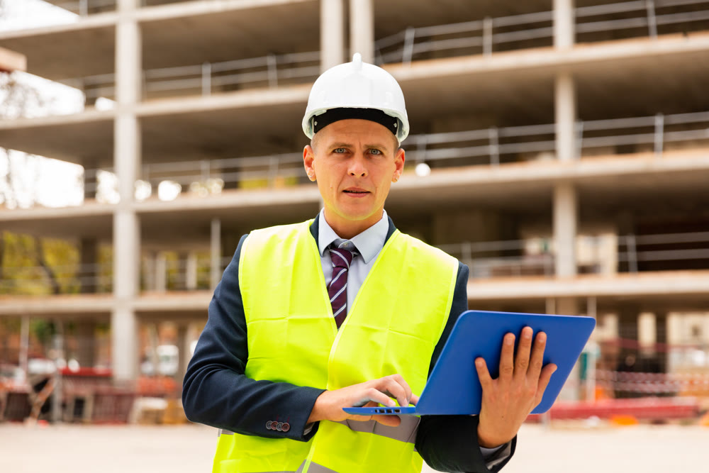 Professional positive man in jacket and helmet working at electonic device outdoor