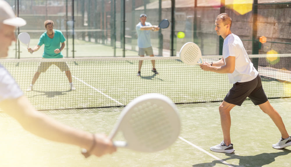 Padel game - man with partners plays on court