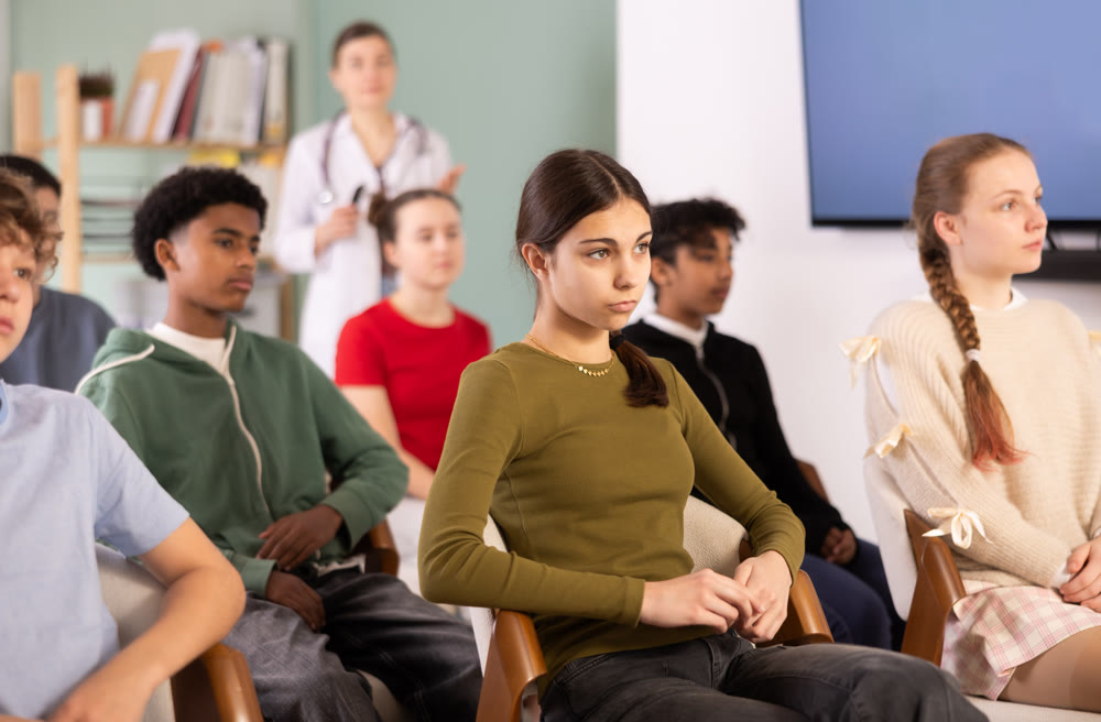 Teenage students listening to lecture while doctor stands in background