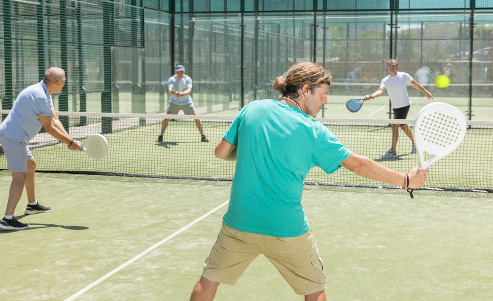 Padel game - man with partners plays on court