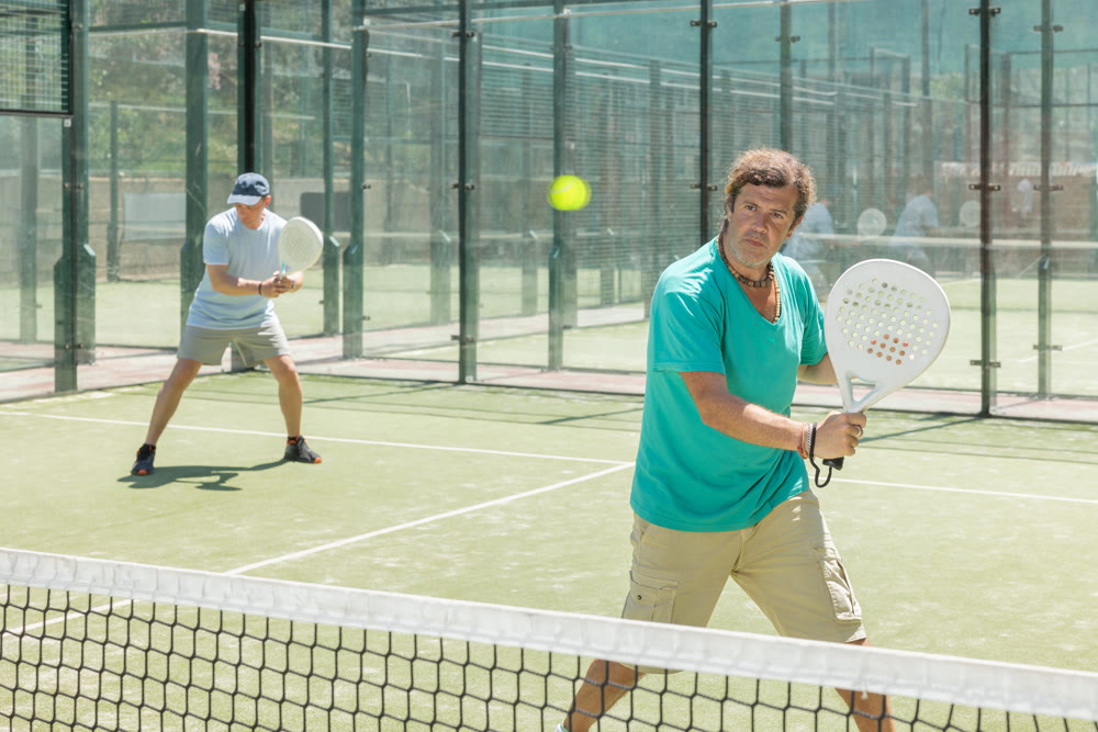 Padel game - man with partners plays on court