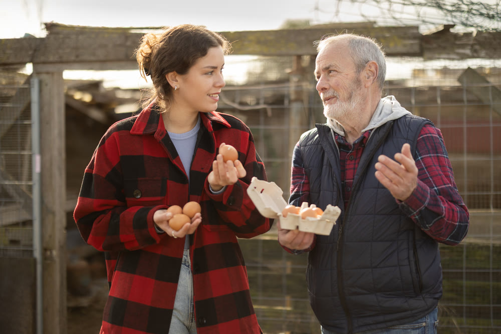 Mature man and young woman holding fresh eggs in chicken coop