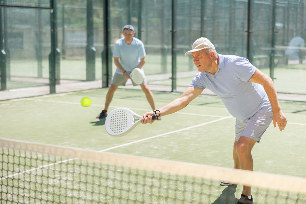 Portrait of sporty mature man playing padel on open court on autumn day, ready to hit ball. Health and active lifestyle concept