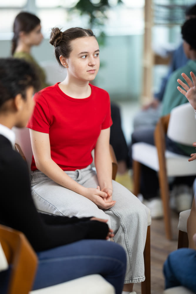 Teenage girl sits in a circle opposite other schoolchildren, they communicate