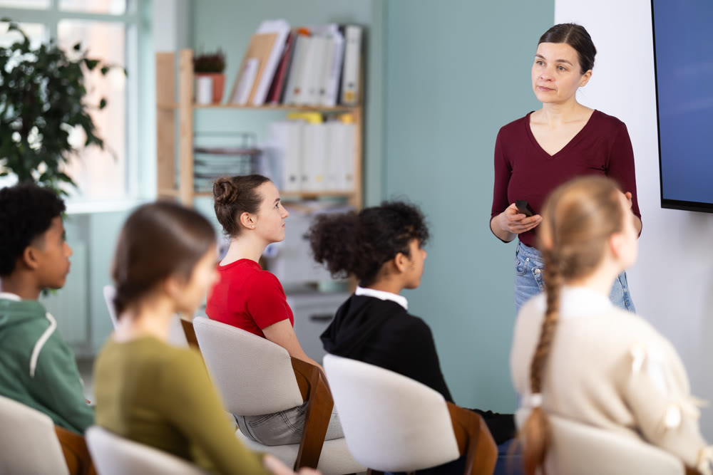 Teacher conducts a lesson in front of a group of students, explaining the material at the screen