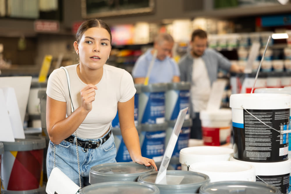 Woman buys jar with paint in paintwork material department of construction store for carrying out internal finishing work on object