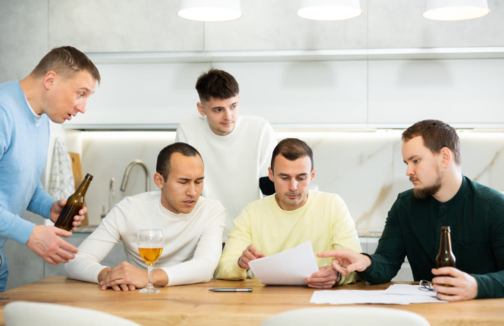 Male friends read a financial or legal document, drink beer and try to solve financial problems by consulting each other while sitting at table