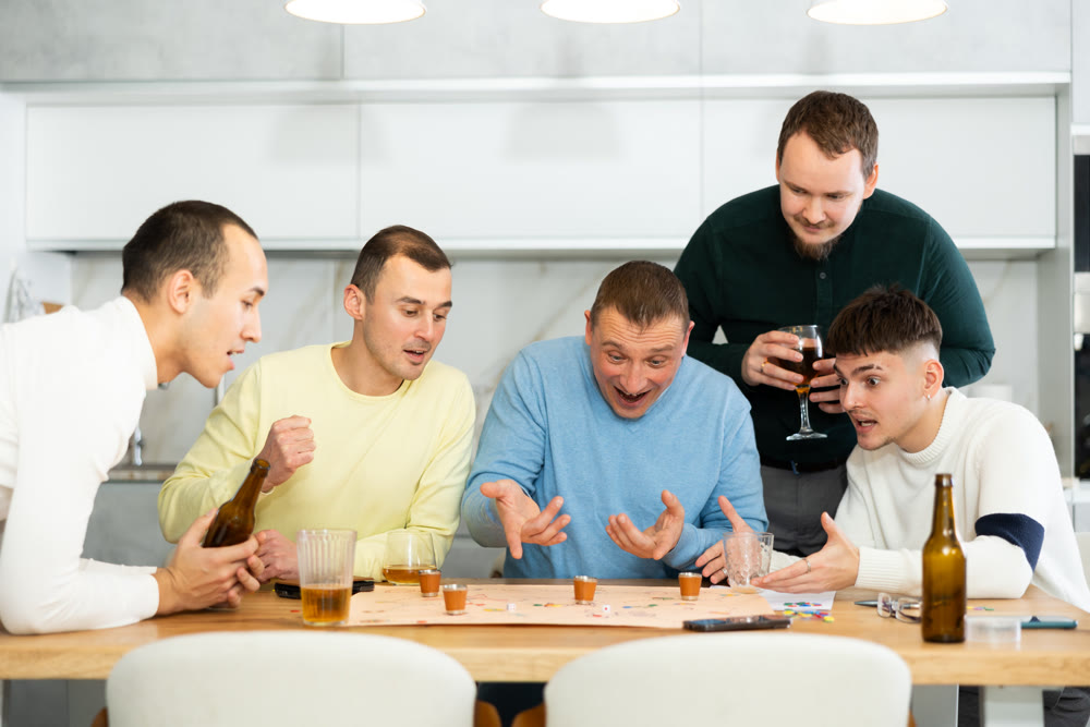Group of cheerful men engaged in alcohol-fueled board game