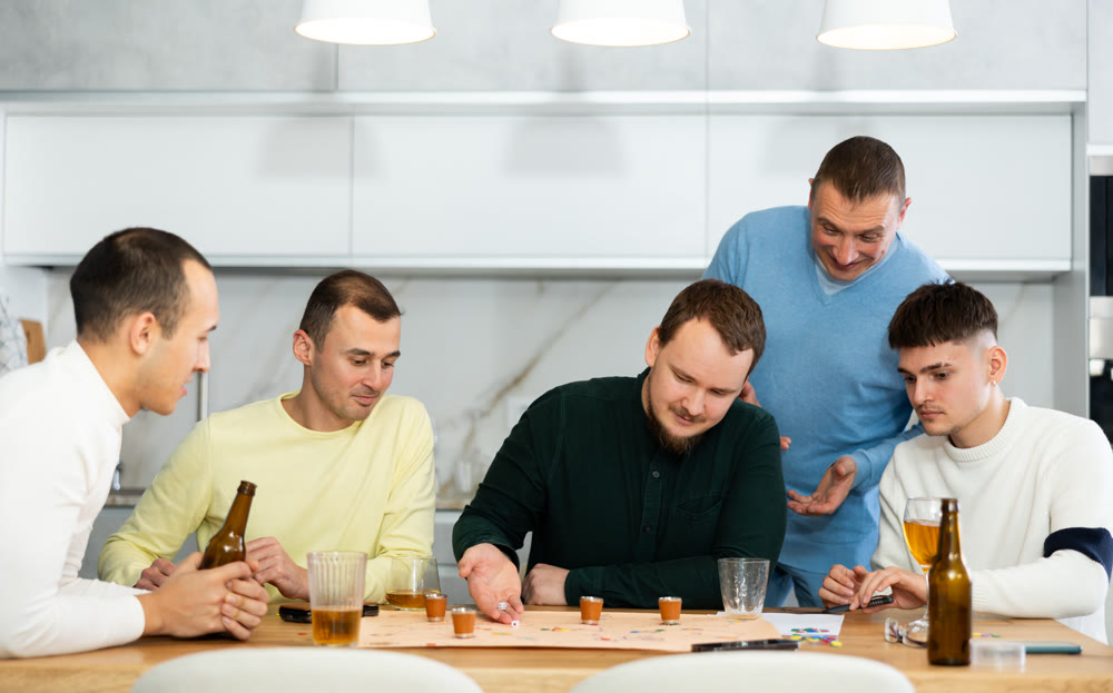 Friends drinking beer and enthusiastically playing board game at home