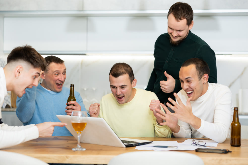 Group of friends watching football match on a laptop together and drinking beer