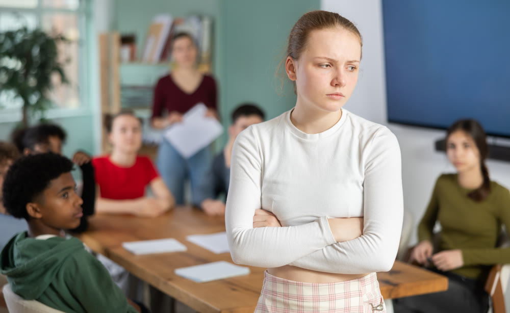 Upset European teenage girl standing in front of the classroom