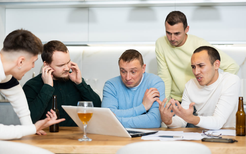 Men drink beer and try to help friend solve problems using laptop and Internet