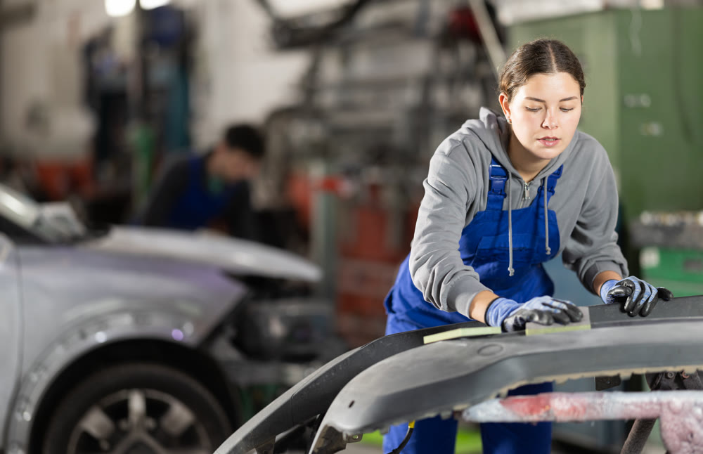 Woman car mechanic polishes car bumper - prepares bumper for painting in car service