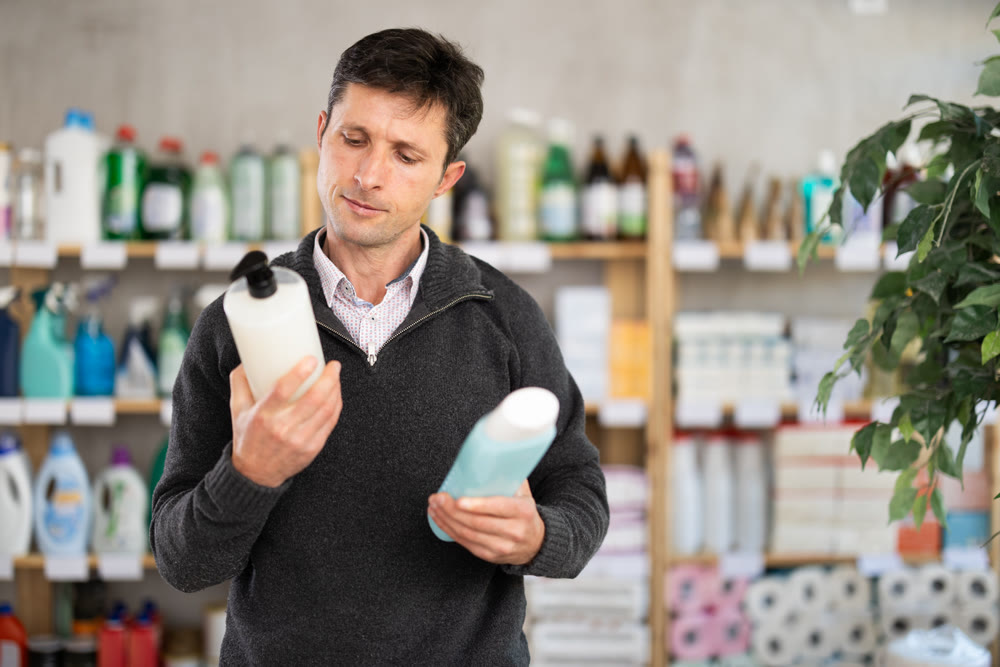 Man buyer chooses shampoo or shower gel in household goods department of supermarket