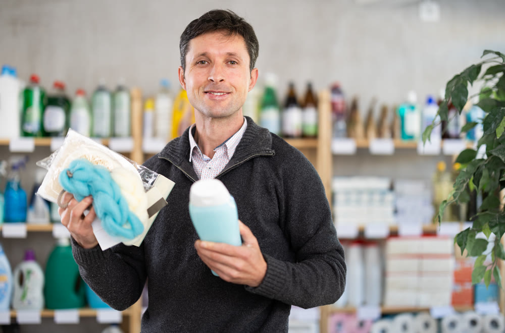 Middle-aged man holding shower gel choosing body washcloth at department store