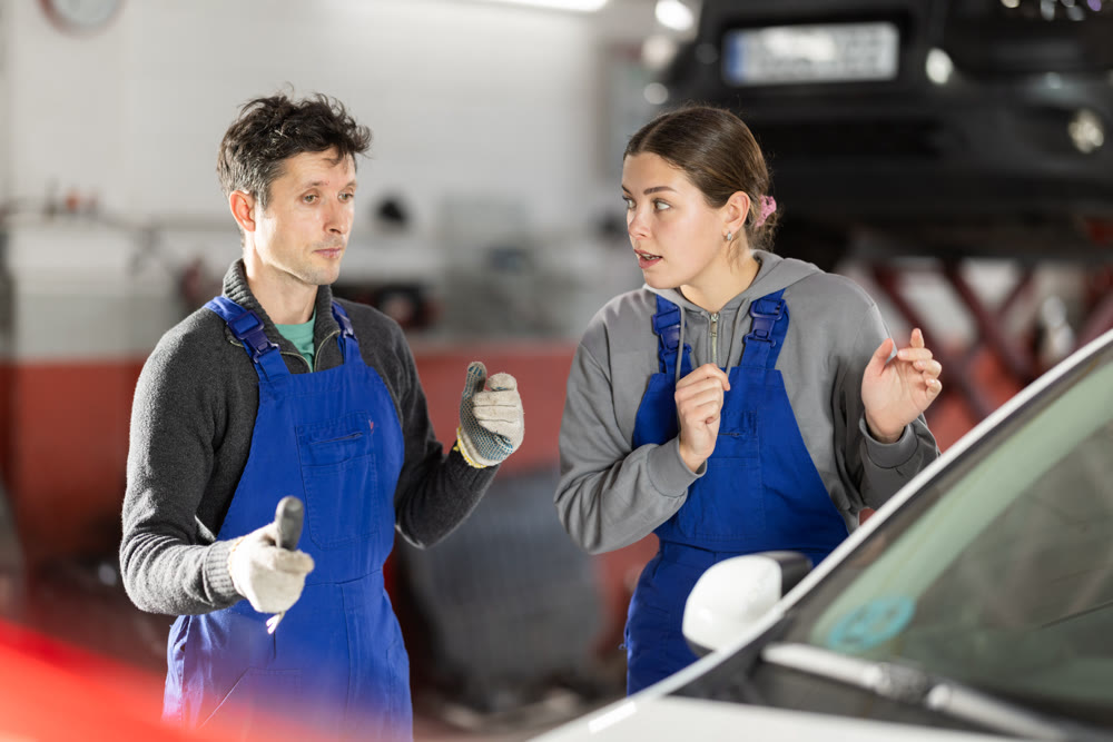 Two auto mechanics, man and woman, diagnosing a car engine together in car repair shop