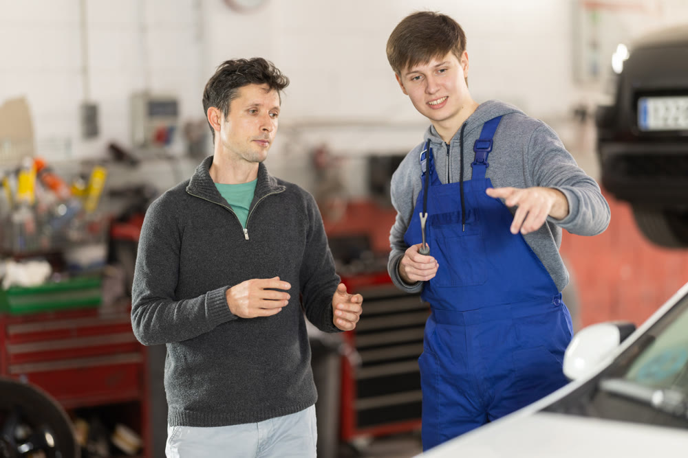 Adult car owner discusses with a young auto mechanic the cost and time of car repairs at car service center