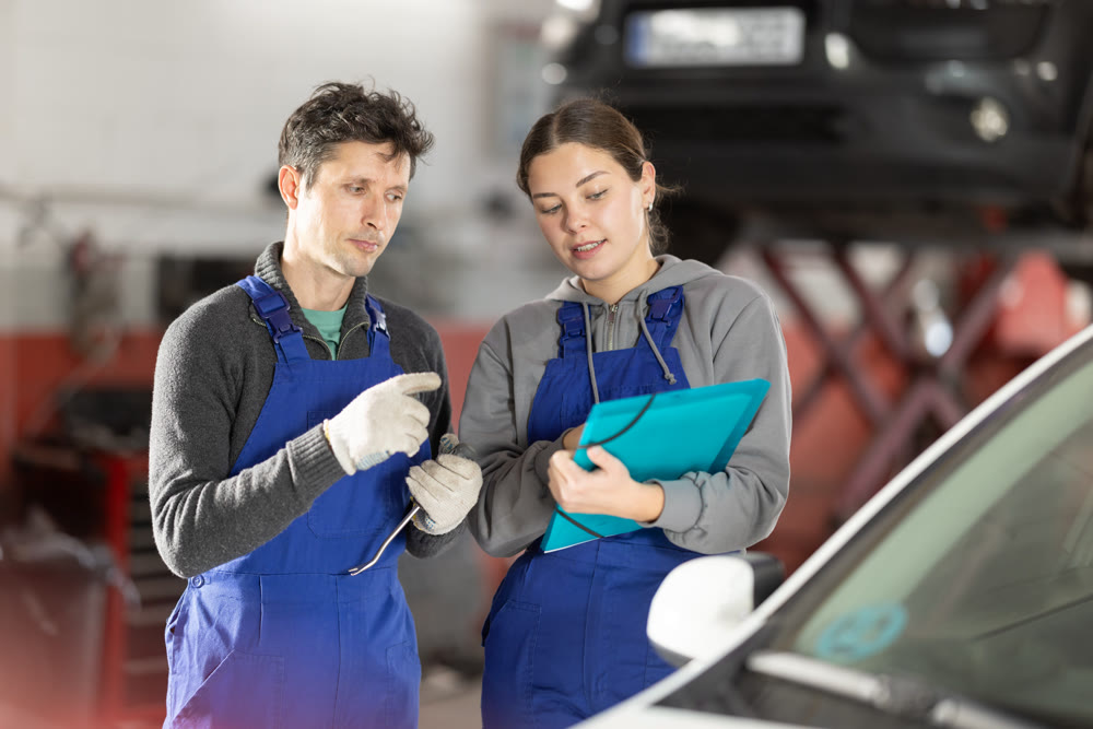 Car service manager discusses car repair problems with mechanic. He takes notes on paper