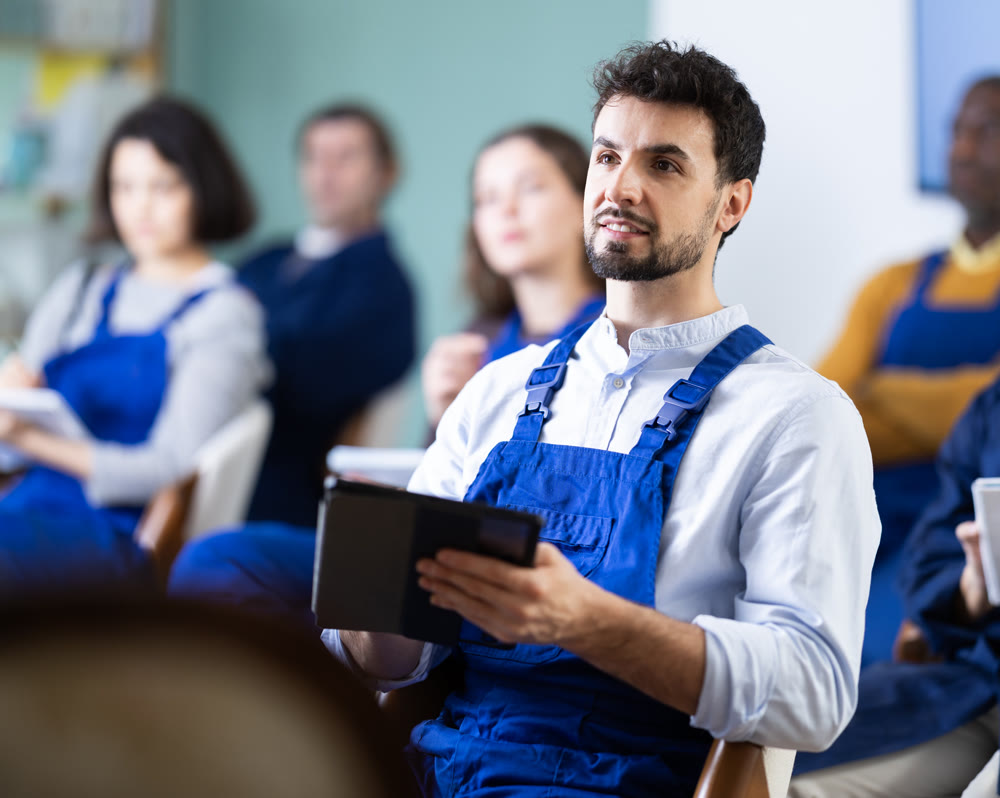 Man in overalls takes notes in an electronic notebook during refresher course