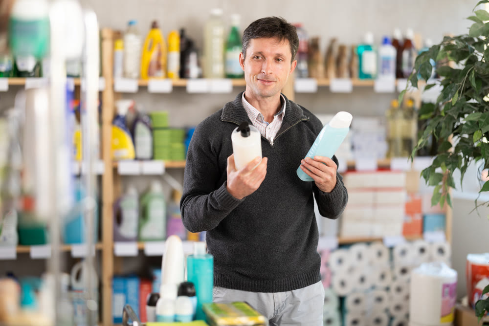 Man buyer chooses shampoo or shower gel in household goods department of supermarket