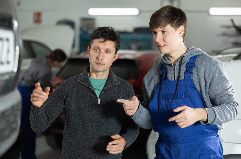 Adult car owner discusses with a young auto mechanic the cost and time of car repairs at car service center
