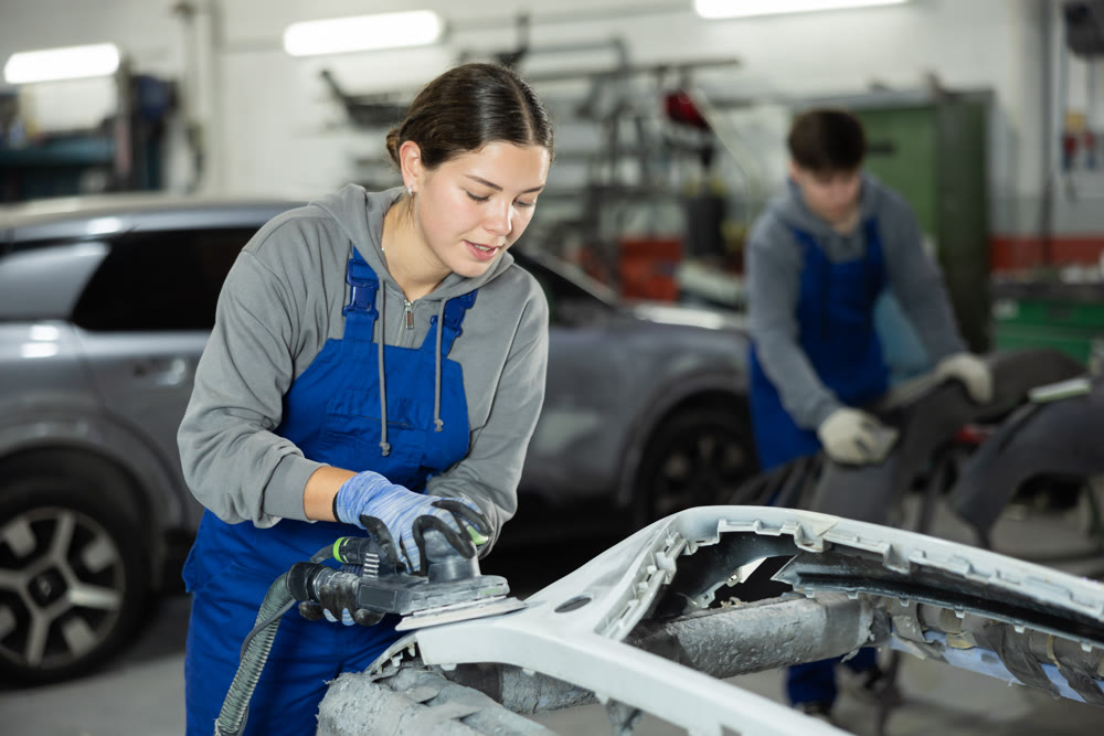 Young woman auto mechanic polishes body parts by car buffer polisher machine tool