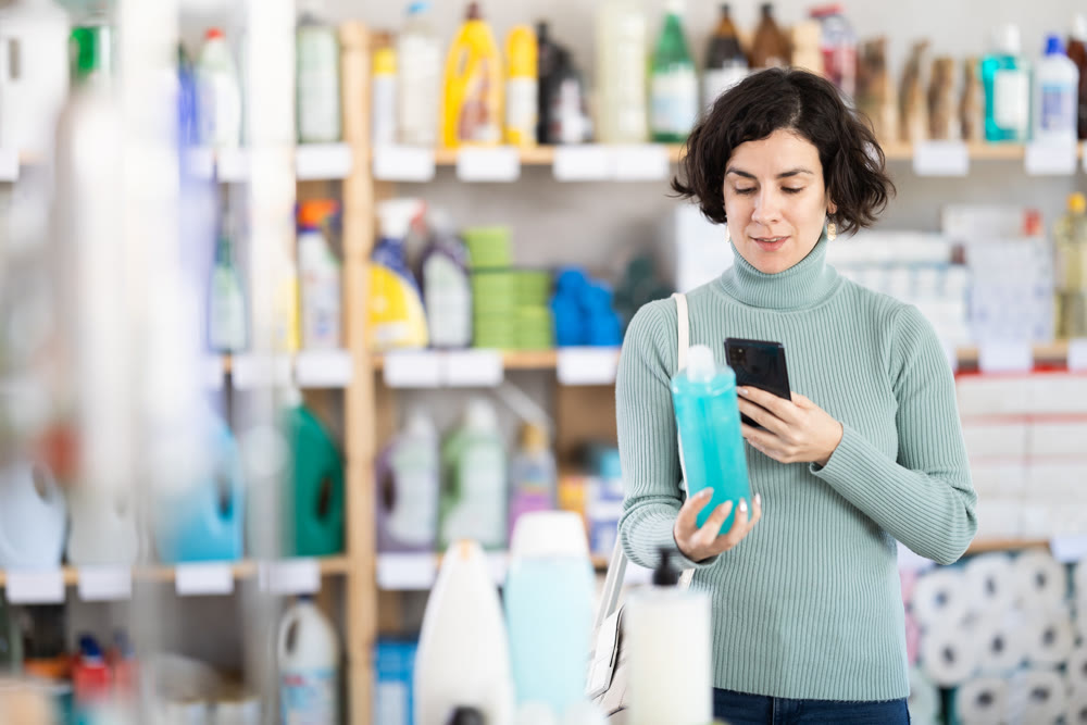 Middle-aged woman scanning QR-code on shampoo at department store