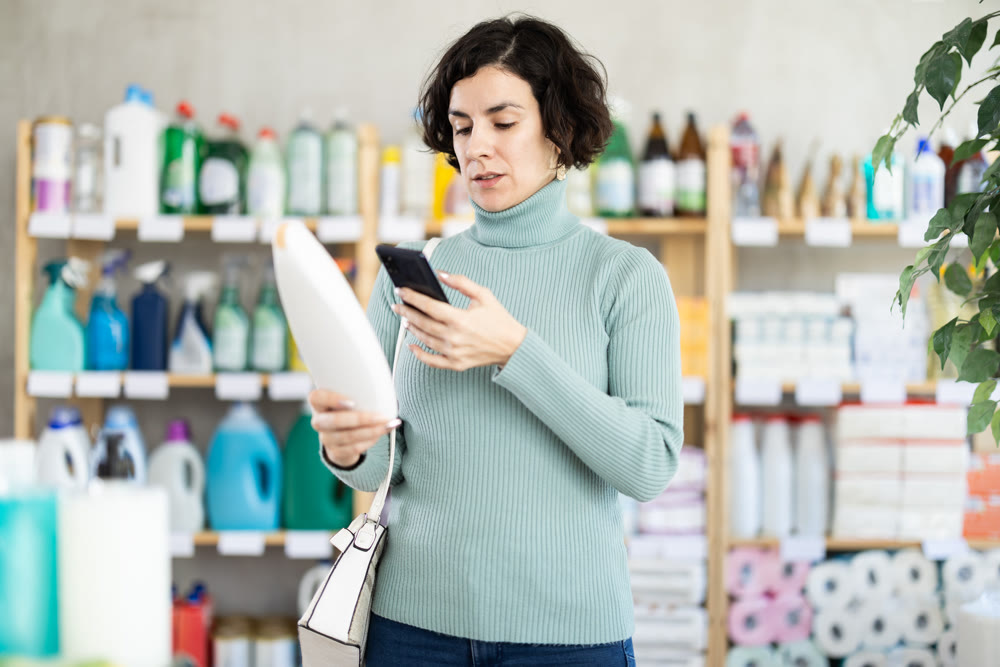 Middle-aged woman scanning QR-code on shampoo at department store