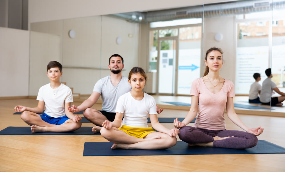 Sporty parents and teenage kids sitting in lotus position in yoga studio