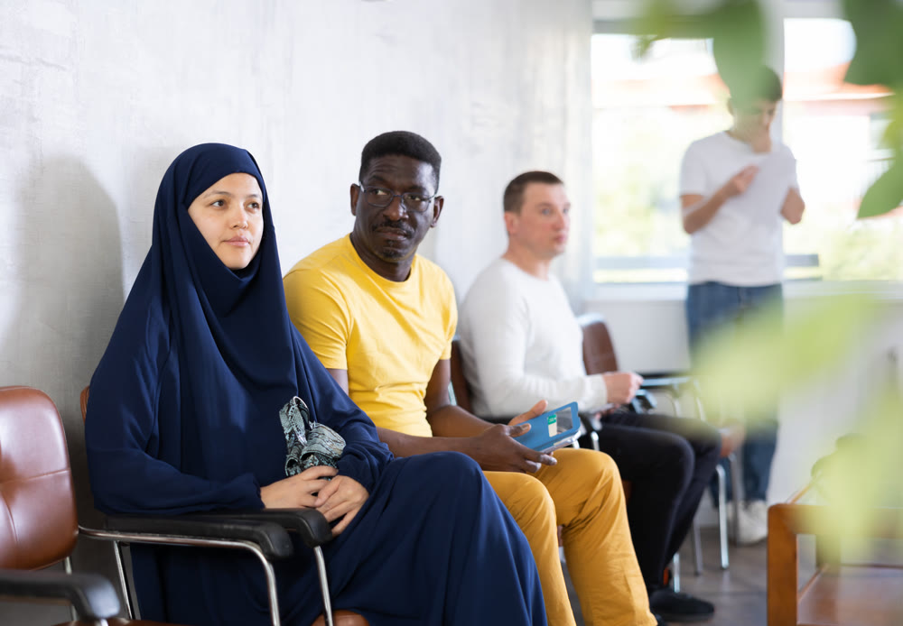 African man talking to Muslim woman sitting in lobby of civil service building