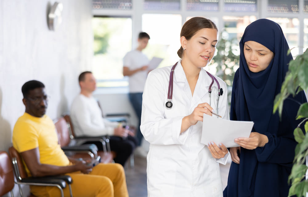 Young female doctor showing papers to Muslim woman in lobby of clinic